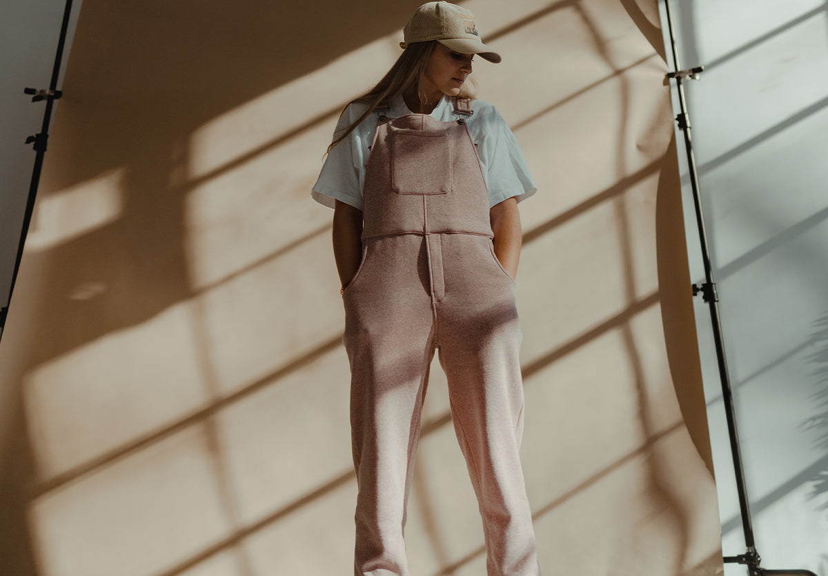 Person wearing Supercomf Swoveralls in Heather Rose standing in front of a tan background