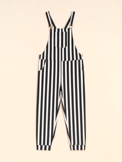 Black and white vertically striped overalls with adjustable shoulder straps and side pockets, displayed flat against a light beige background.