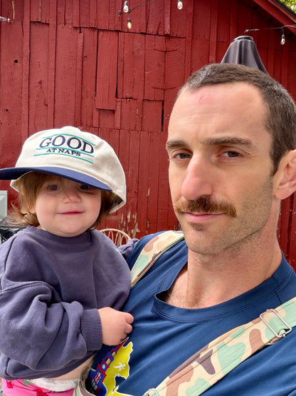 Toddler wearing the cream and navy Good at Naps cap outdoors