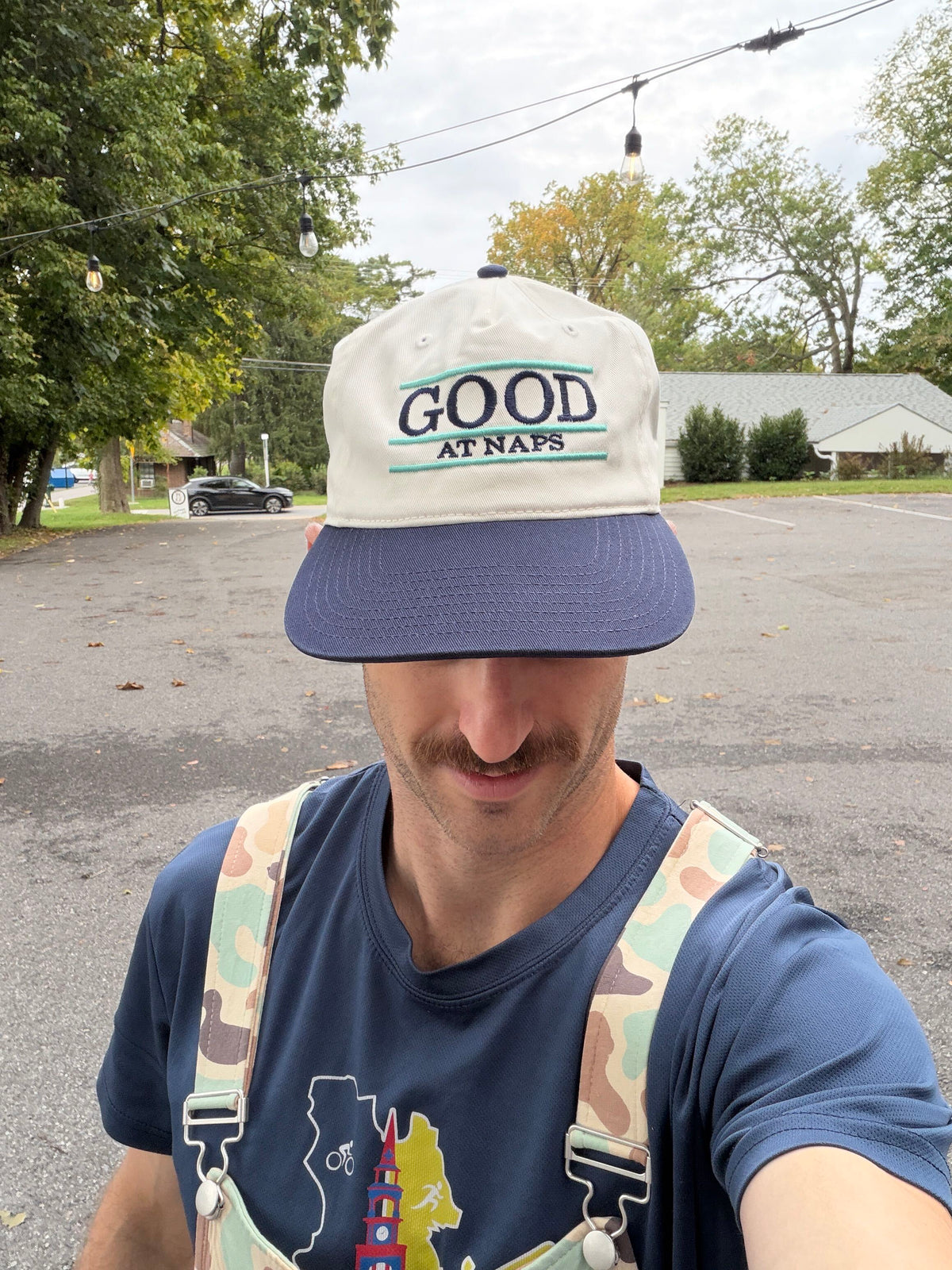 Front view of the cream and navy Good at Naps cap with teal stripe embroidery