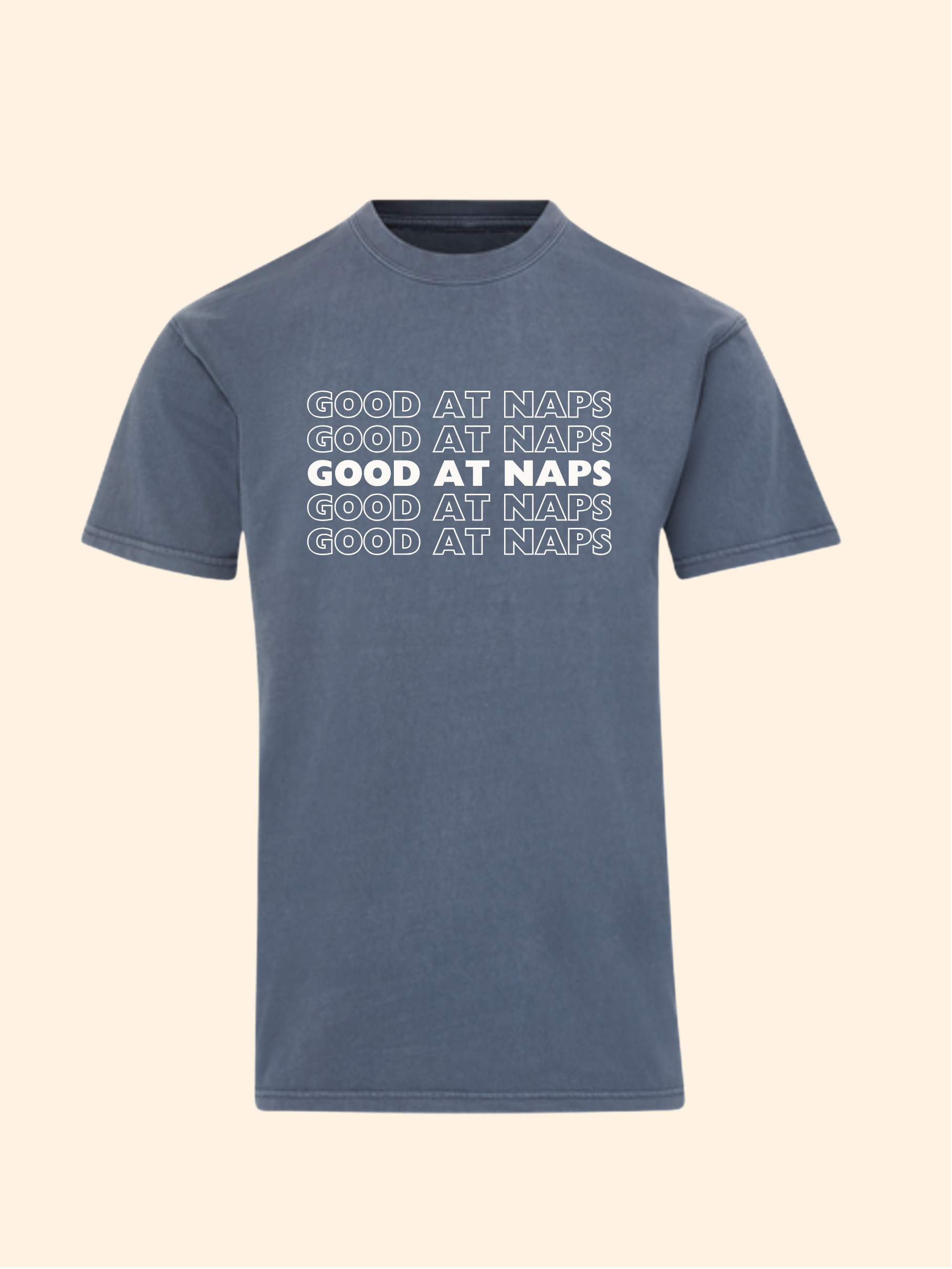 A slate blue short-sleeve t-shirt with 'GOOD AT NAPS' printed in white across the chest in a stacked, shadowed design, shown against a solid cream background.