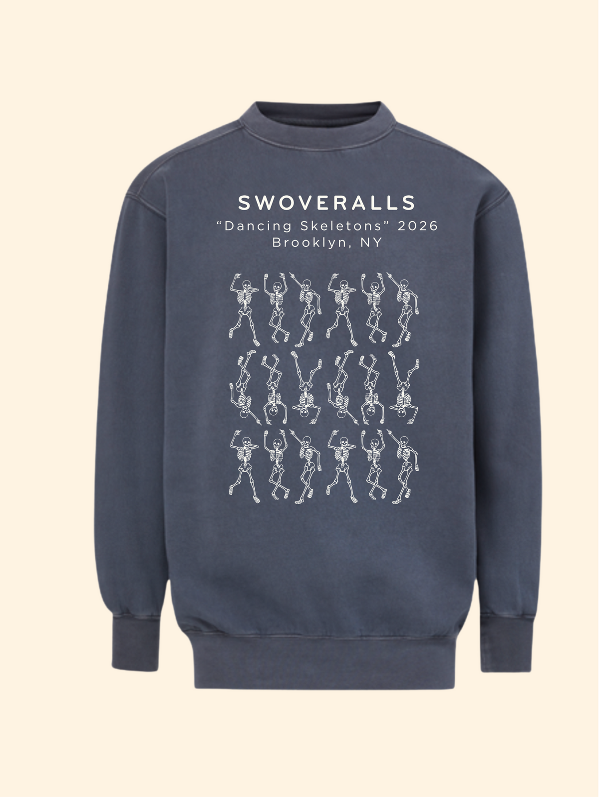 A dark slate blue crewneck sweatshirt featuring a white graphic print of the text 'SWOVERALLS "Dancing Skeletons" 2026 Brooklyn, NY' above a grid of dancing skeleton figures, shown against a solid cream background.