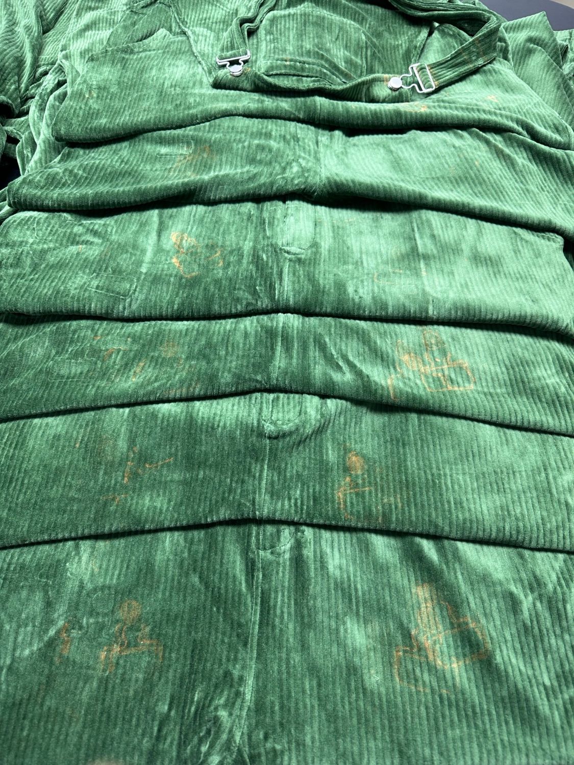 Stack of Perfectly Imperfect Forest Green corduroy Swoveralls showing light rust-colored marks on the fabric