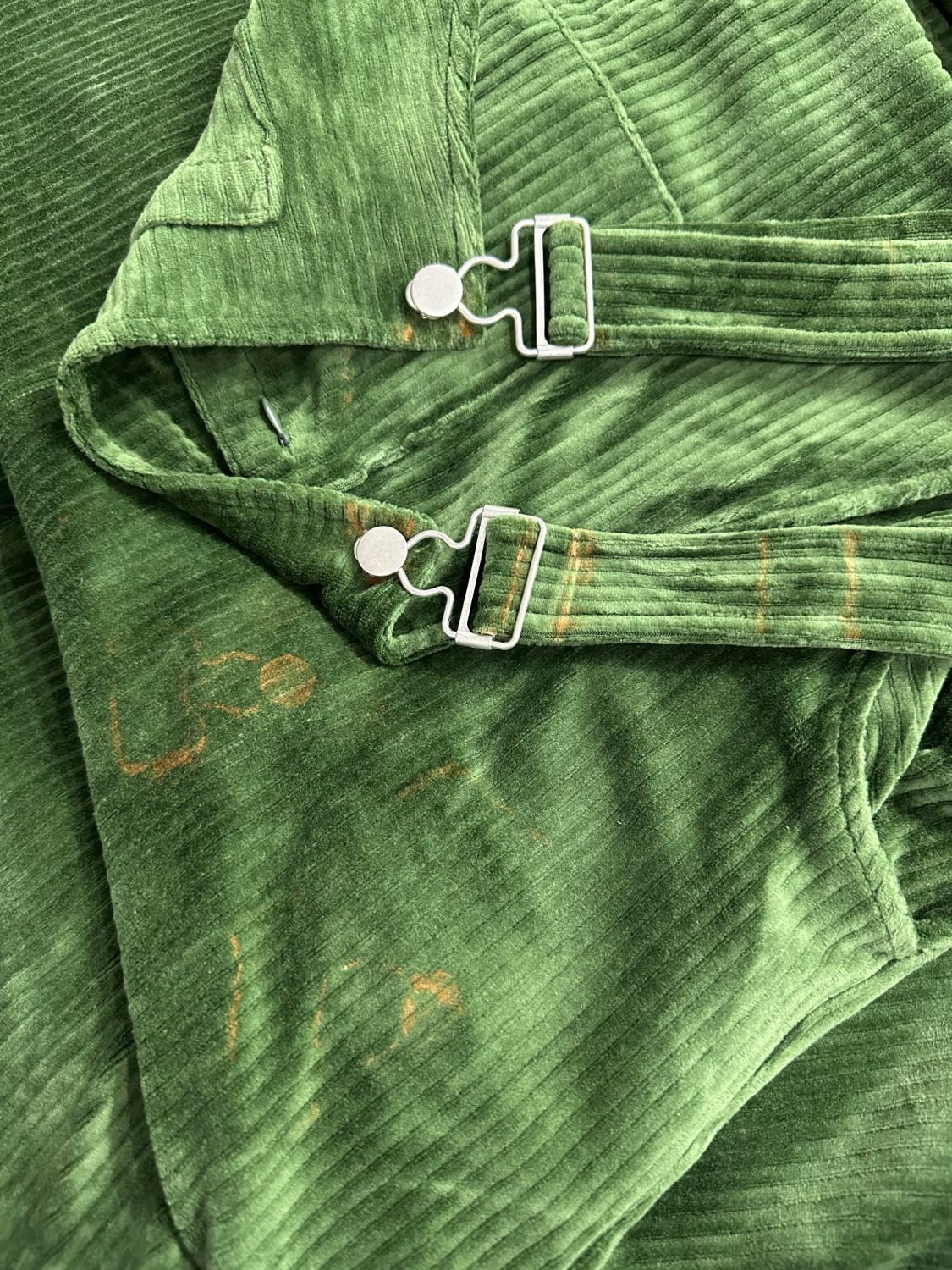 Close-up of the bib and strap buckles on Perfectly Imperfect Forest Green corduroy Swoveralls with rust-colored marks