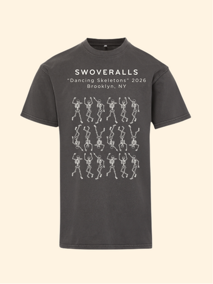 A dark charcoal gray t-shirt with a graphic print on the front. The print features the text 'SWOVERALLS Trash Pandas 2026 Brooklyn, NY' above a pattern of raccoons in a trash can with small colorful details.