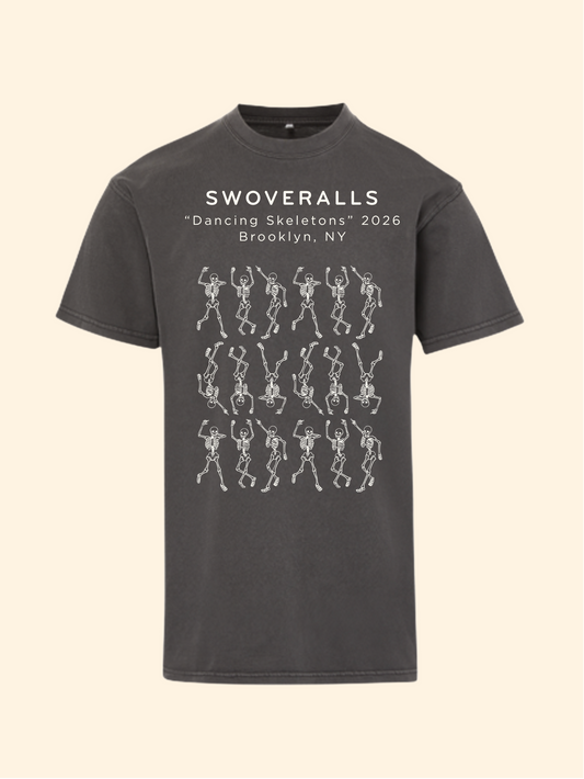A dark charcoal gray t-shirt with a graphic print on the front. The print features the text 'SWOVERALLS Trash Pandas 2026 Brooklyn, NY' above a pattern of raccoons in a trash can with small colorful details.